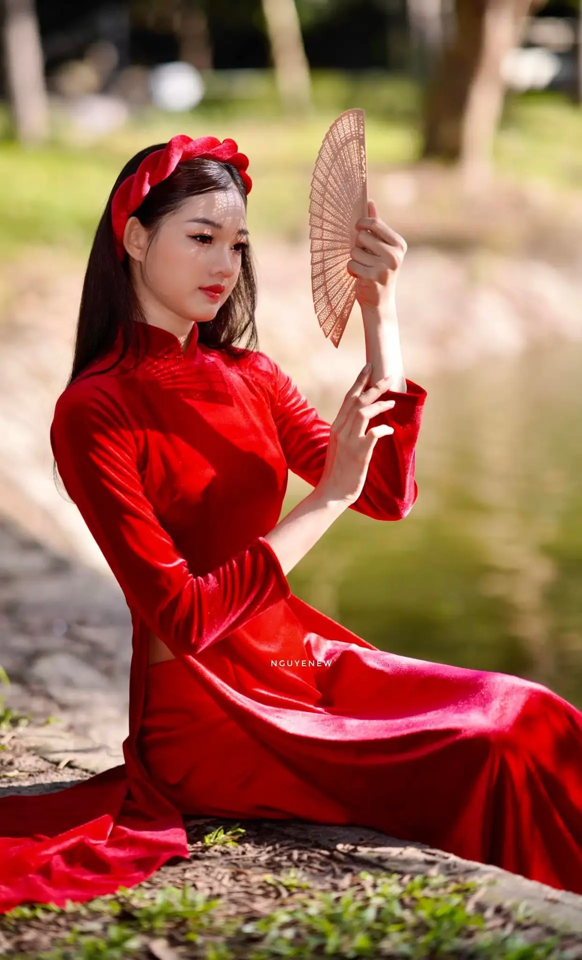Discover the enchanting beauty of a Vietnamese woman in a traditional Red Ao Dai by the tranquil water.