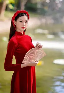 Discover the enchanting beauty of a Vietnamese woman in a traditional Red Ao Dai by the tranquil water. - image 1